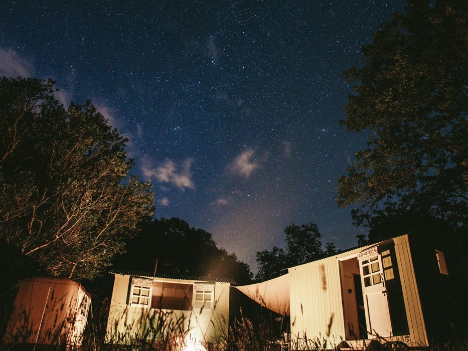 The shepherds' huts are lit up by the firepit in the foreground with the starry skies of Snowdonia Dark Sky Reserve overhead