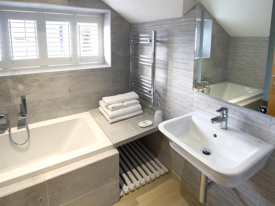 Elegant bathroom with a deep bathtub, heated towel rail, and modern basin set against stone-effect tiles.