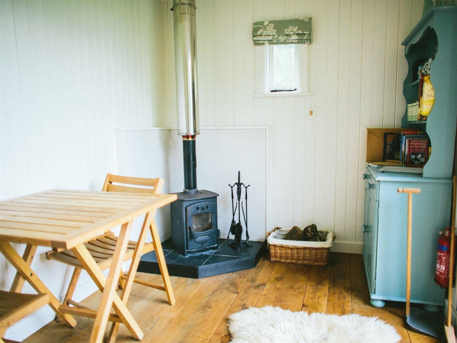The inside of the shepherd's hut with sheepskin rug on the oak floor, blue welsh dresser, wood-burning stove with a basket of logs and a small oak tab