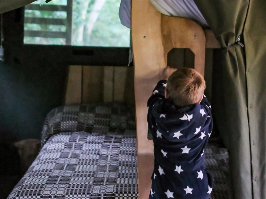 A child climbing up into a bunkbed in a safari tent.