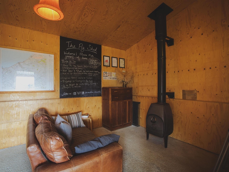 A plywood lined room with a large brown sofa facing a wood burning stove.