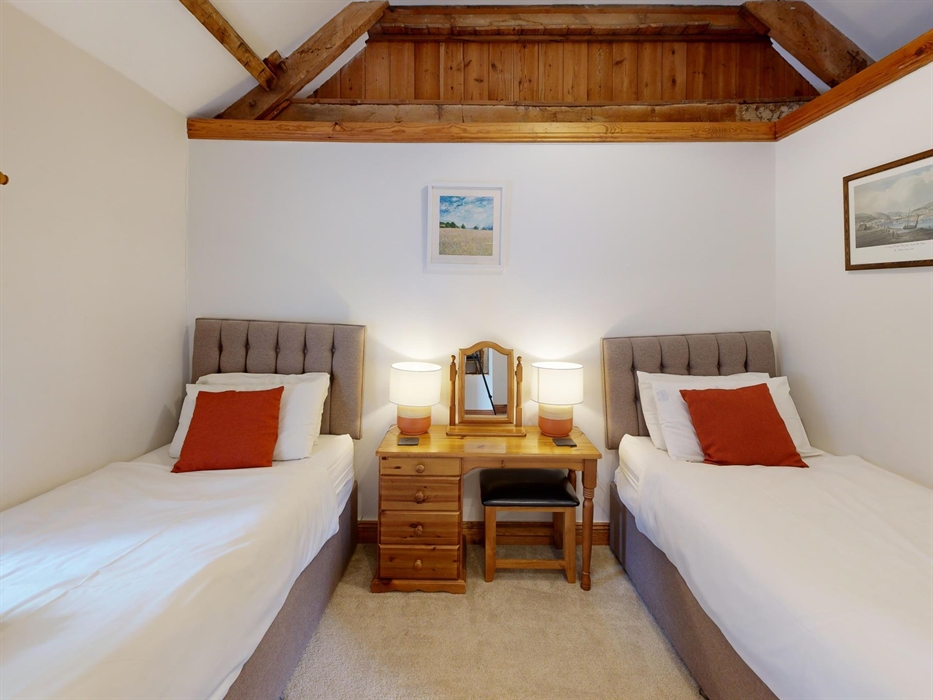 Twin beds with burnt orange cushions and a central dressing table beneath sloped ceiling and beams.
