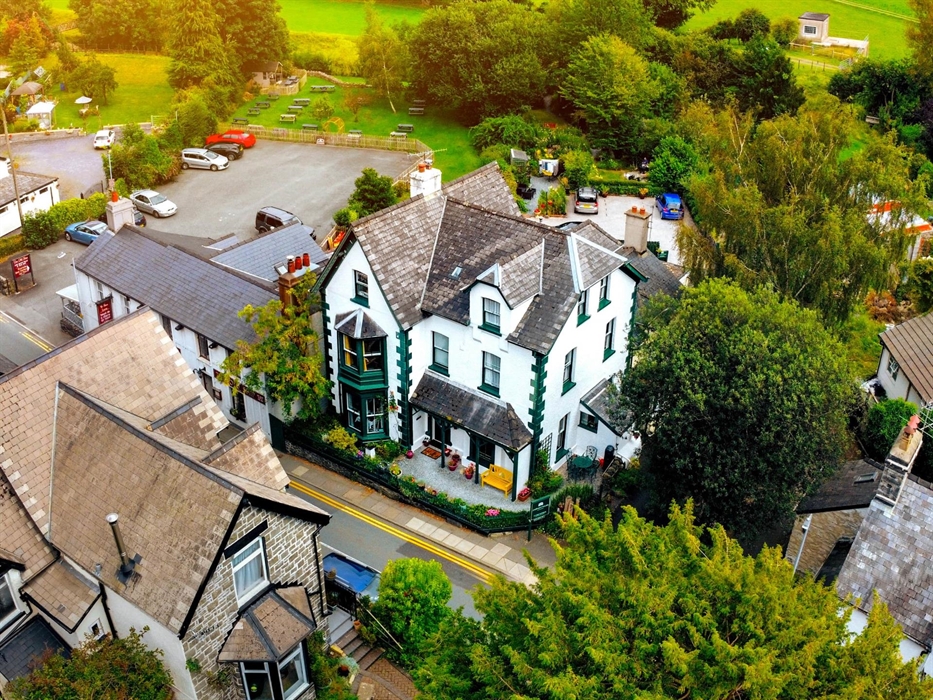 Large white and green house in Trefriw, North Wales seen from above surrounded by green trees and with green fields behind it