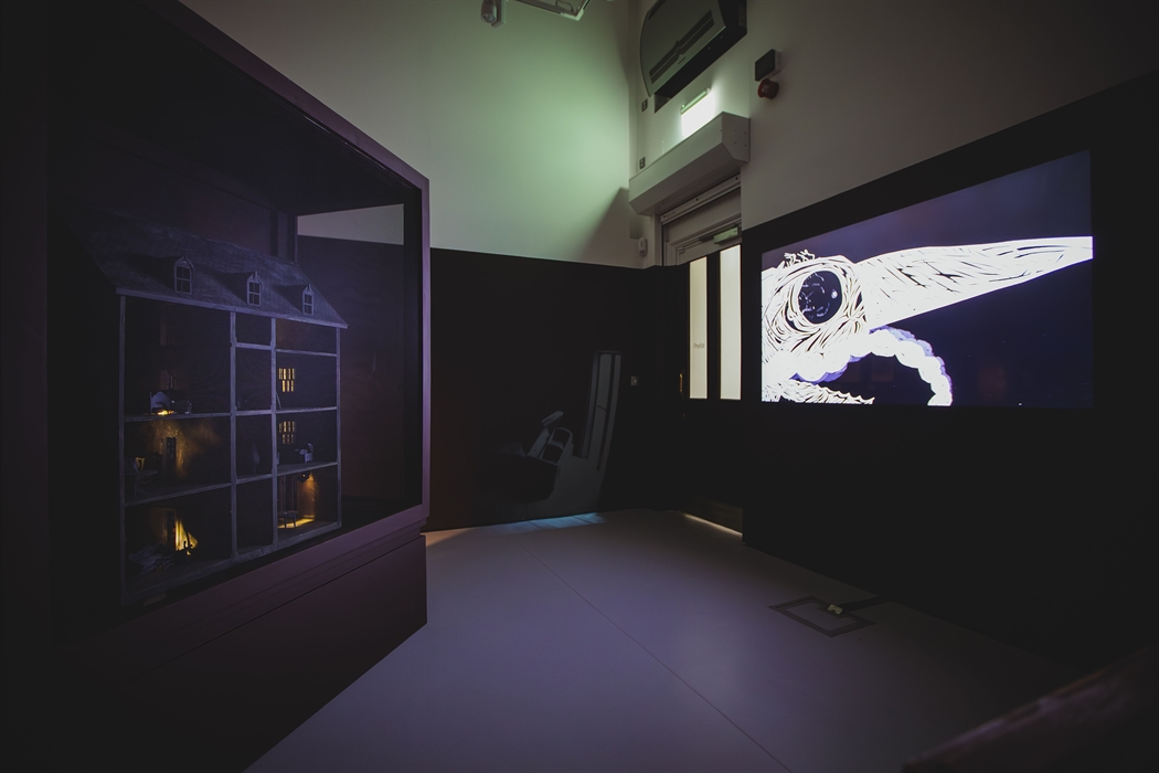 A dark and moody room with an eerie dolls house and animation playing on a tv screen.