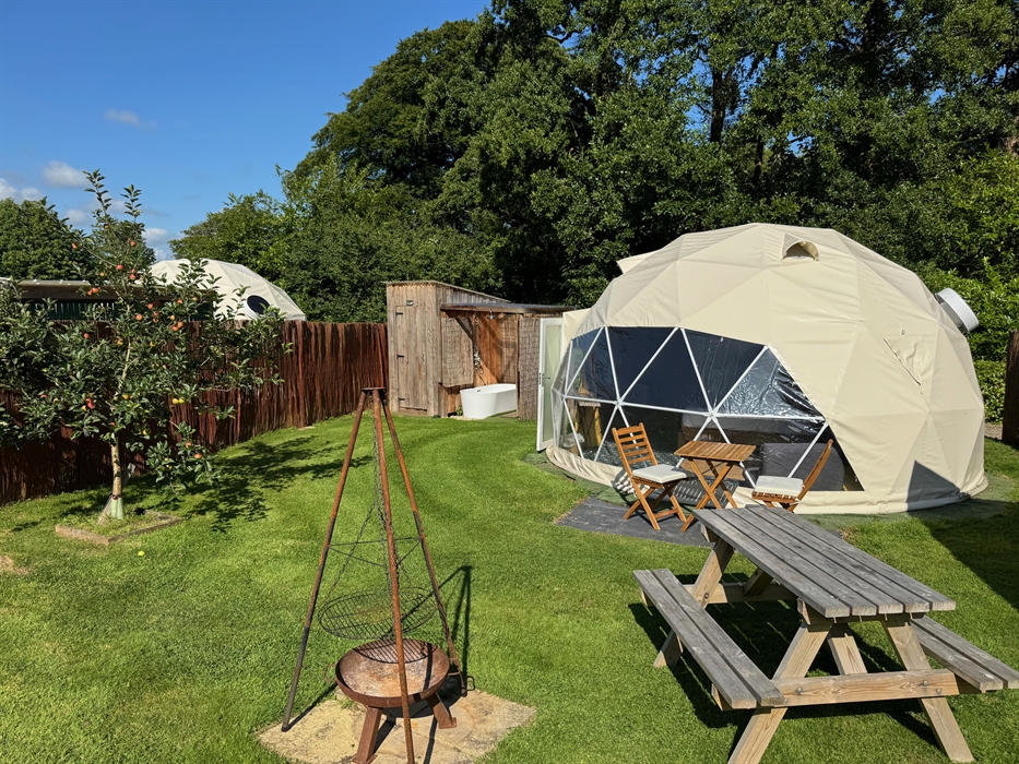 A 5m dome, fully insulated, set in its own garden with picnic table, Firepit and outdoor furniture. An open air deep bathtub can be seen in the backgr