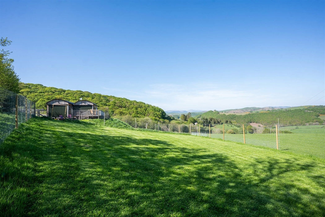 At the end of the hut garden, looking back towards the hut. Quarter of an acre grassy garden fenced at 6ft 4 high / 1.93m. Garden is on a slope, and h