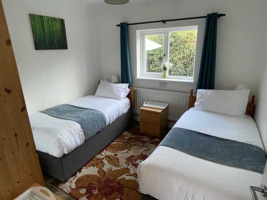 Twin bedroom with 2 full size single beds, 2 bedside cabinets, mirror wardrobe and window overlooking the private garden area