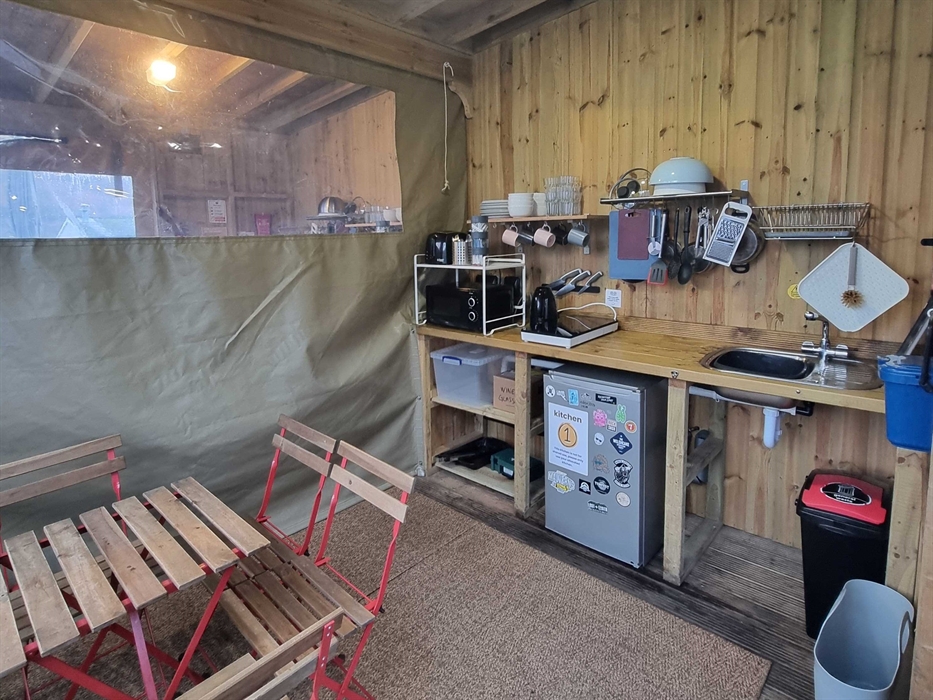A wooden room with table and chairs and kitchen equipment including a fridge and microwave