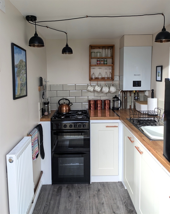 Black gas stove with hob top kettle, boiler, sink and black counter top fridge.Magnetic knife rack on wall. , copper tea, coffee,sugar canisters.