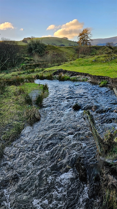 The meandering river flowing through the valley surrounded by lush green rolling countryside