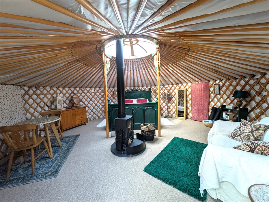 The yurt is round with many painted wood rafters radiating from the central roof light. There is a central logburner on a round slate hearth. At the b