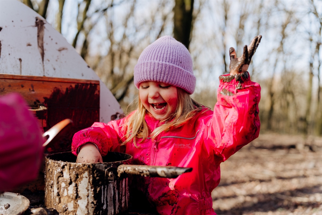 A child laughs as they play in the mud kitchen at WWT Llanelli