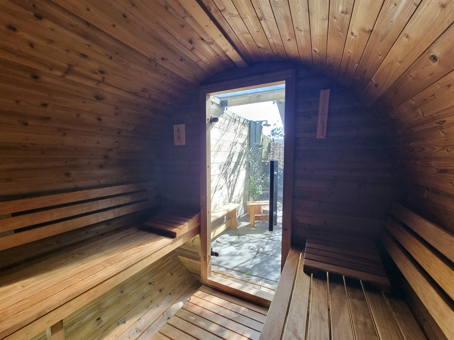 Inside a wooden barrel shaped sauna with wooden benches and a glass door to the outside