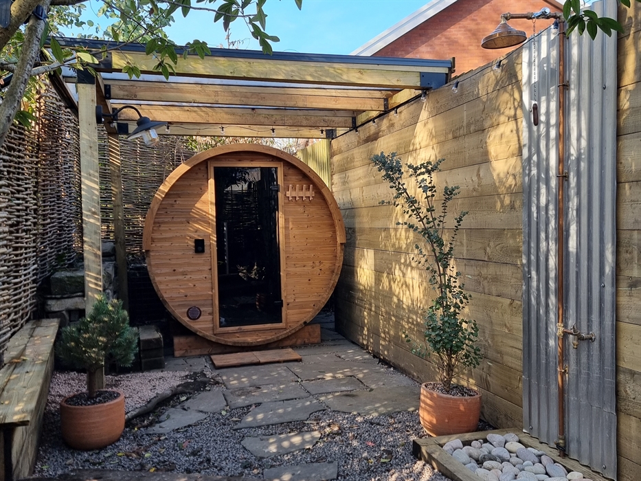 A round wooden barrel sauna with a glass door and benches for sitting on and an outdoor shower