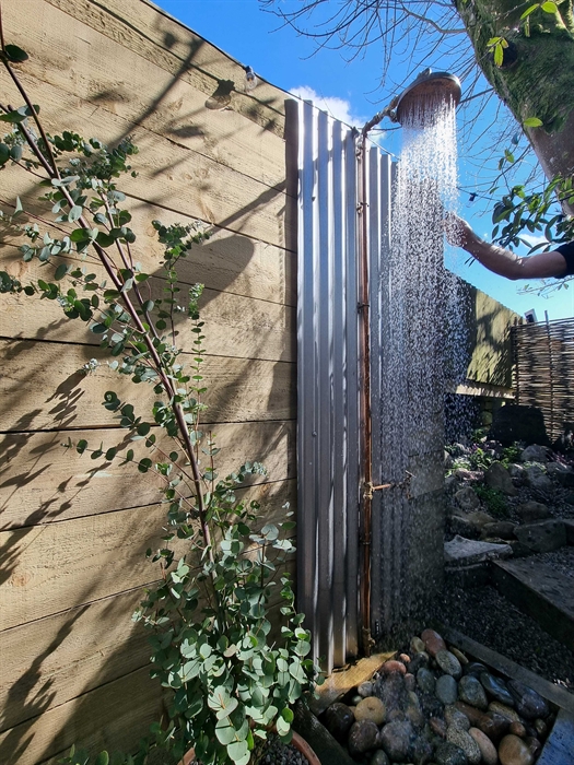 An outdoor shower raining down water against a blue sky with a eucalyptus tree