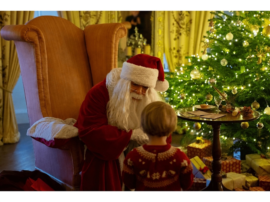 Father Christmas with a child infront of a decorated Christmas tree surrounded by presents.