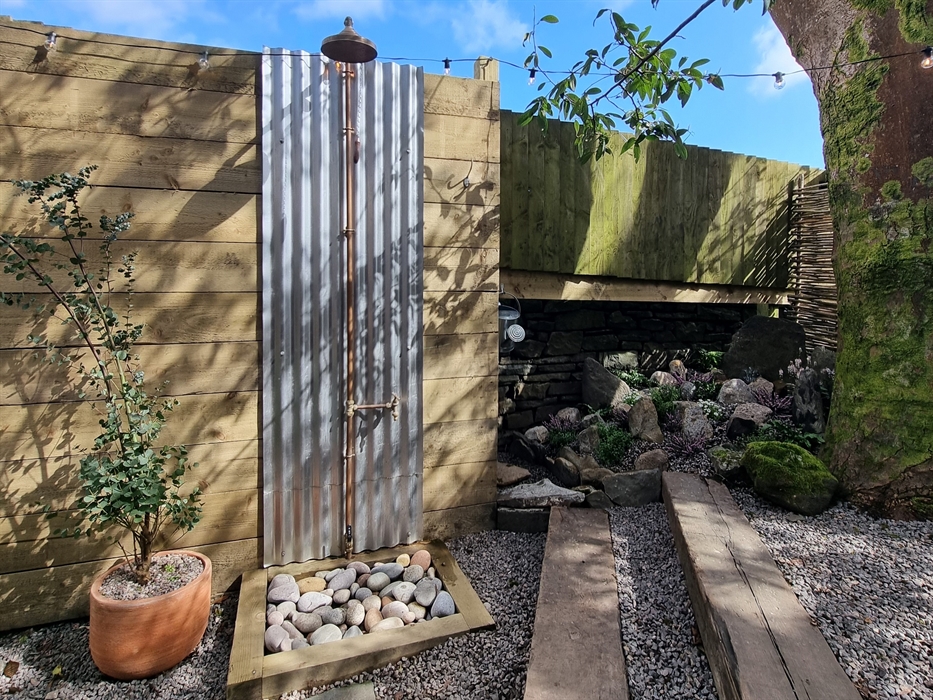 An outdoor shower next to a eucalyptus tree in a pot