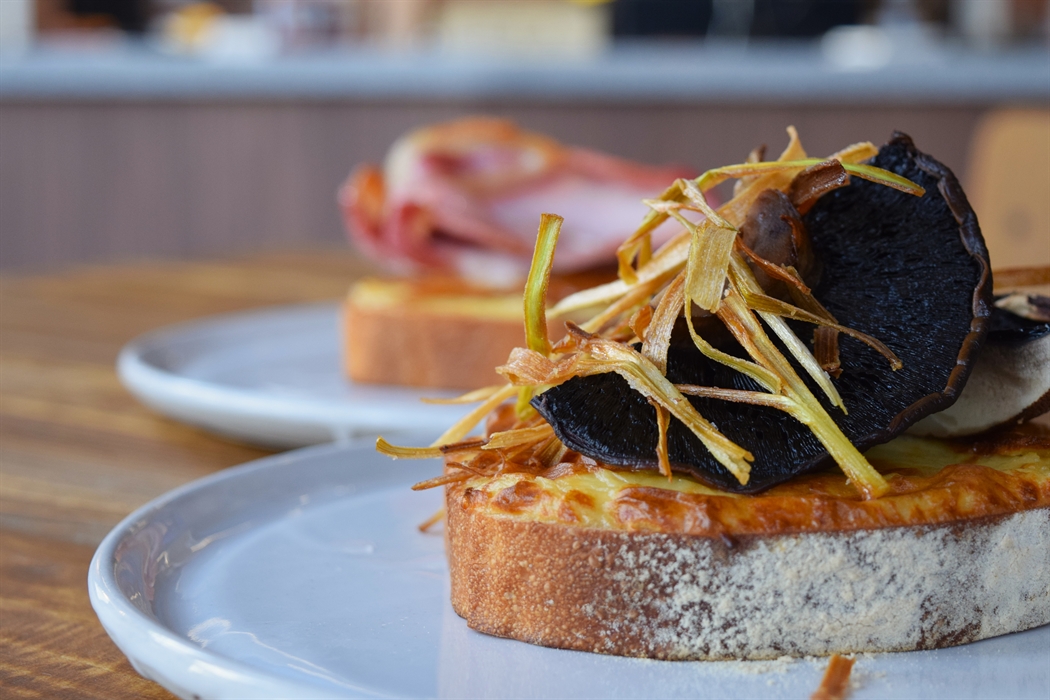 A close up picture of a Welsh Rarebit meal, topped with crispy onions and large mushrooms on white crusty bread.