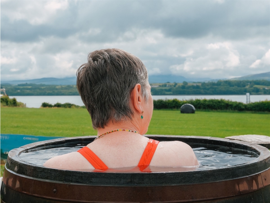 An image of a woman bathing at Halen Môn's Wild Môn Seaweed Baths, bathing in a 40c barrel with views across Eryri.