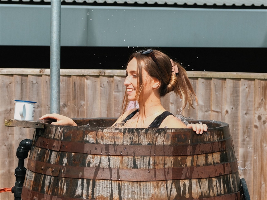 Young woman in a Halen Môn Wild Seaweed Bath, splashing in the barrel with a Halen Môn drink to hand, in the sunshine