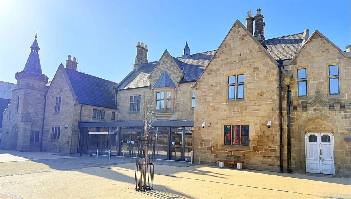 Honey coloured stone building with gravel forecourt in the sunshine with a blue sky