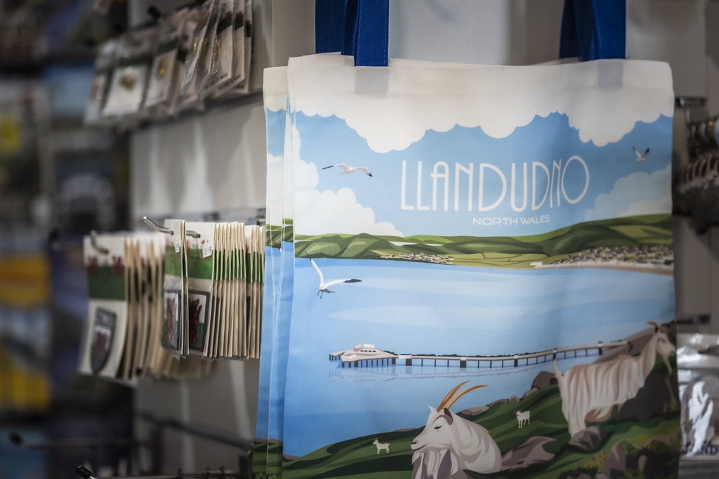Reusable Llandudno shopping bags featuring an illustrated North Wales coastal design displayed in the gift shop.