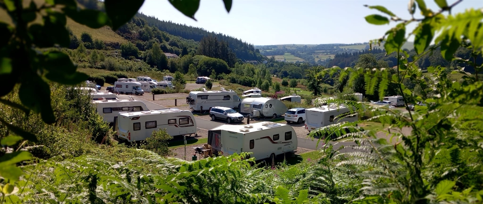 A photo of a woman relaxing on holiday, sat out on a sun lounger reading a magazine overlooking the Clywedog Valley.