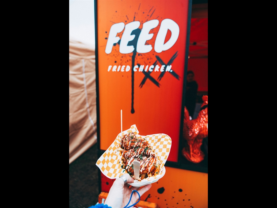 Loaded fried chicken and chips street food served in a takeaway tray at a food festival, with Feed Fried Chicken stall sign in the background.