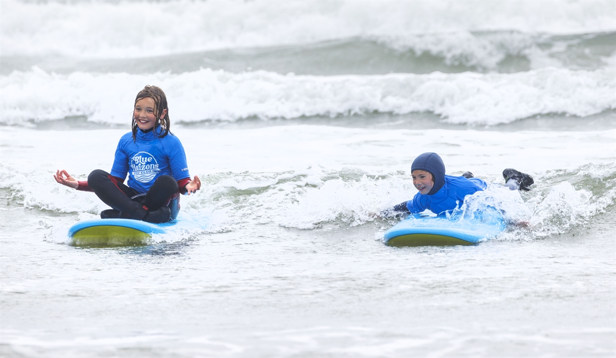 Children learning to surf with Blue Horizons on a Pembrokeshire beach, smiling in small waves