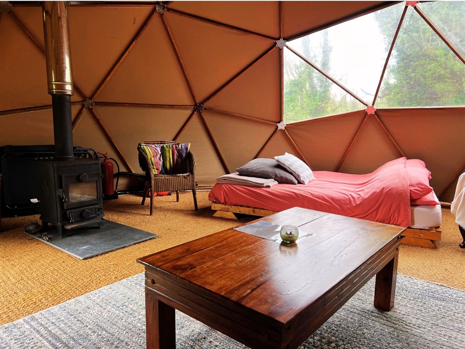 Geodome interior: woodburner, double bed, coffee table, wicker chair