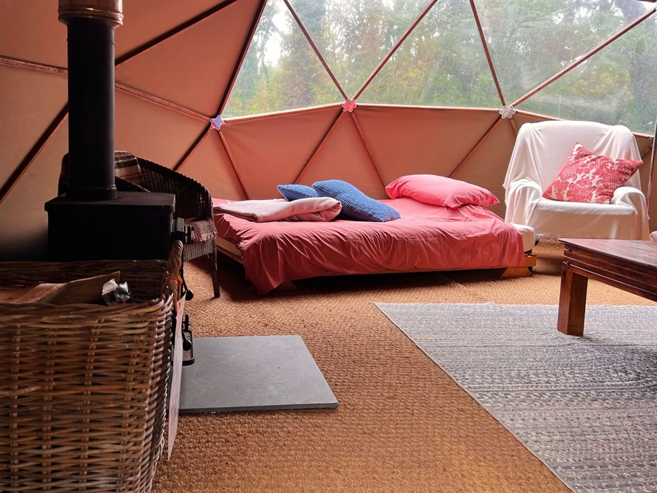 Geodome interior: woodburner, log basket, double bed, coffee table, comfy armchair