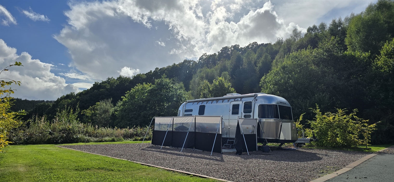 A photo of a woman relaxing on holiday, sat out on a sun lounger reading a magazine overlooking the Clywedog Valley.