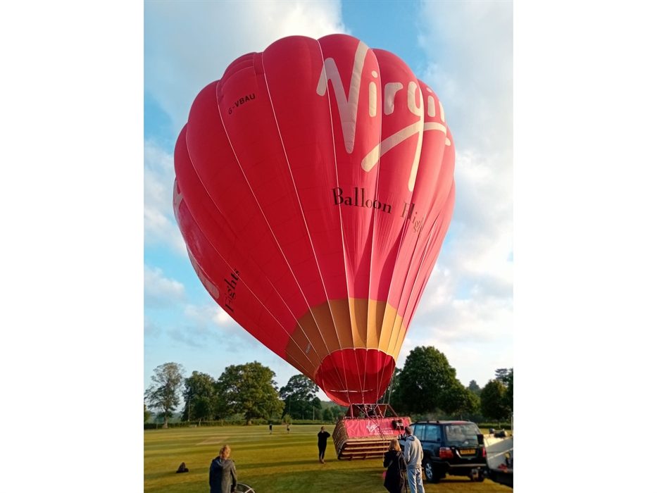 Red Virgin Balloon Flights hot air balloon preparing for take-off on a grassy launch field for a hot air balloon ride in Wales.