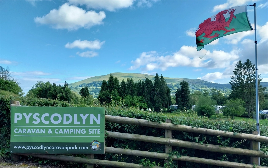main entrance sign at Pyscodlyn caravan site with welsh flag flying and Blorenge Mountain in the distance
