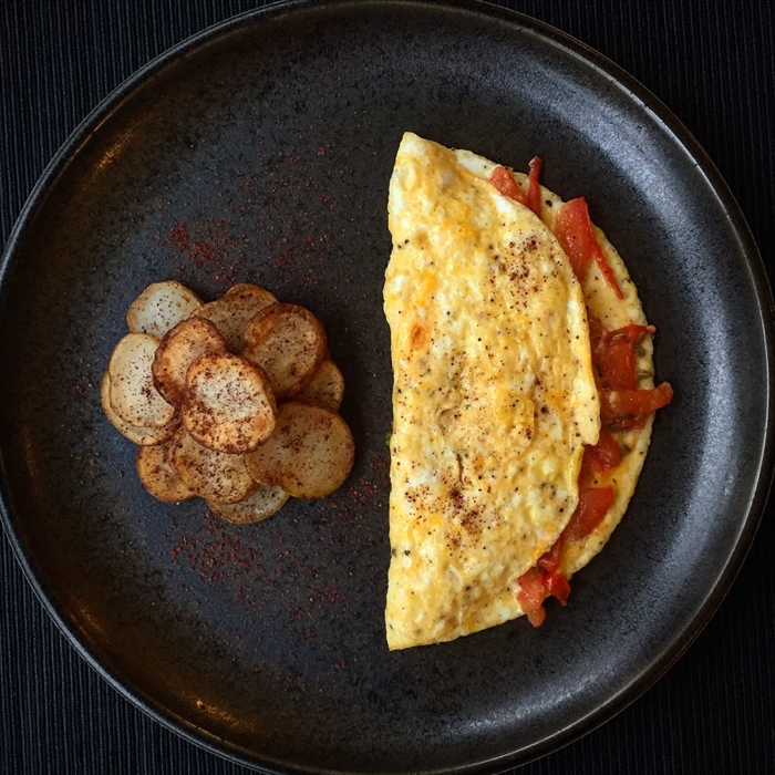 An omelette on a black plate next to a small pile of potatoes