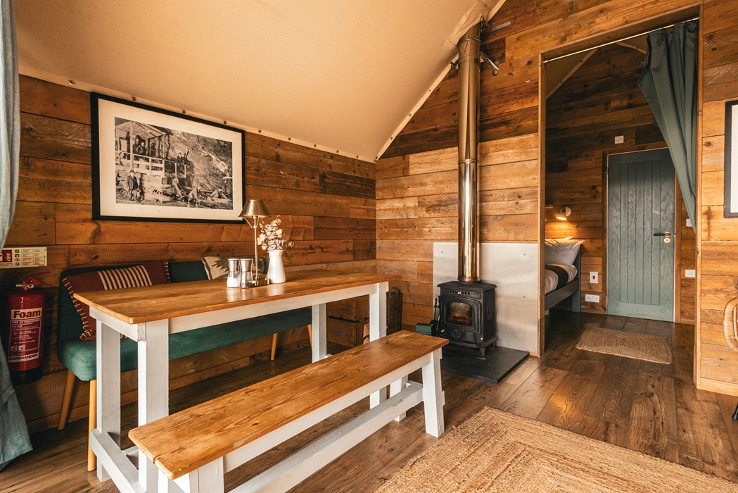 interior of llechwedd glamping tent with dining area, log burner or stove, and bedroom area with bathroom door